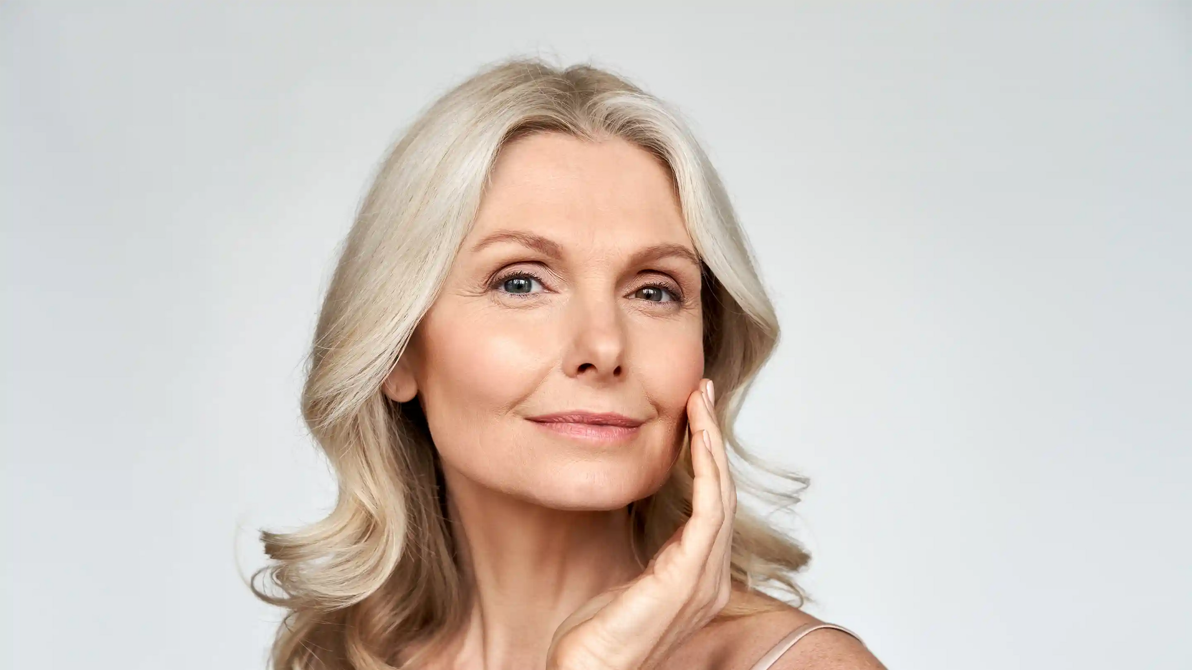 Woman with blonde hair touching her left cheek with her fingers